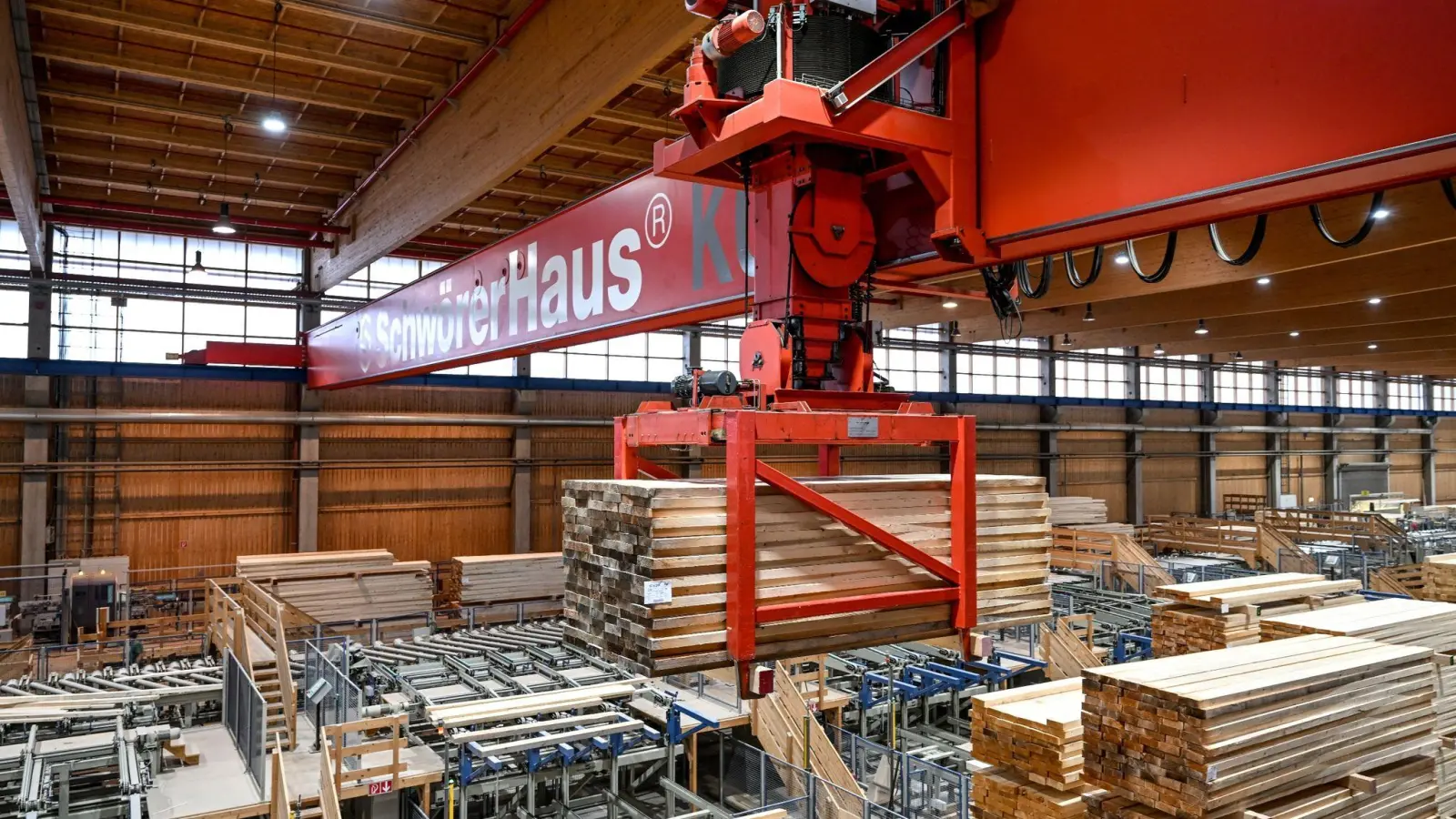 Ein Kran hebt eine Ladung Holz an, um diese in einer Halle der SchwörerHaus KG zu einem anderen Platz zu transportieren. (Foto: Felix Kästle/dpa)