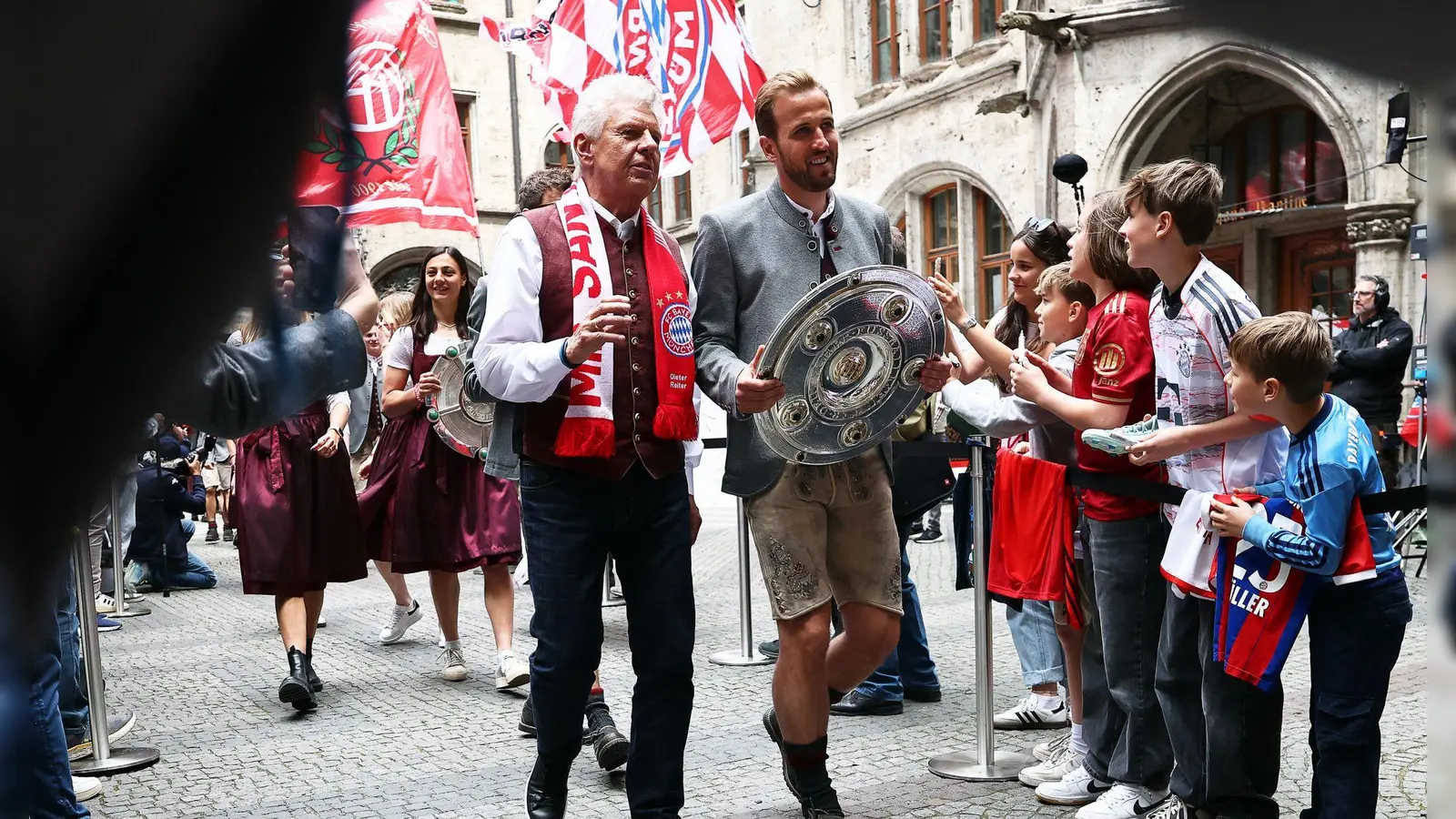 Bundesliga-Torschützenkönig Harry Kane trägt die Meisterschale flankiert von Oberbürgermeister Dieter Reiter (mit Fanschal) ins Münchner Rathaus. (Foto: Daniel Löb/dpa)