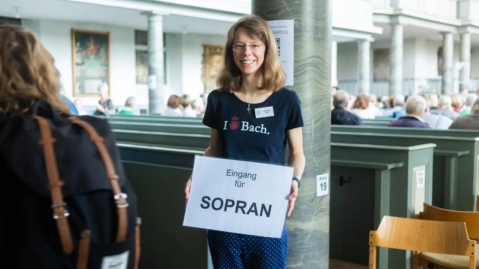 Bei „Ansbach singt” in St. Gumbertus wird das Publikum zur Singgemeinde. Die Sitzordnung ist anders als gewohnt. Bachwochen-Helferin Johanna Dörr sorgt dafür, dass die Soprane den richtigen Platz finden. (Foto: Evi Lemberger)