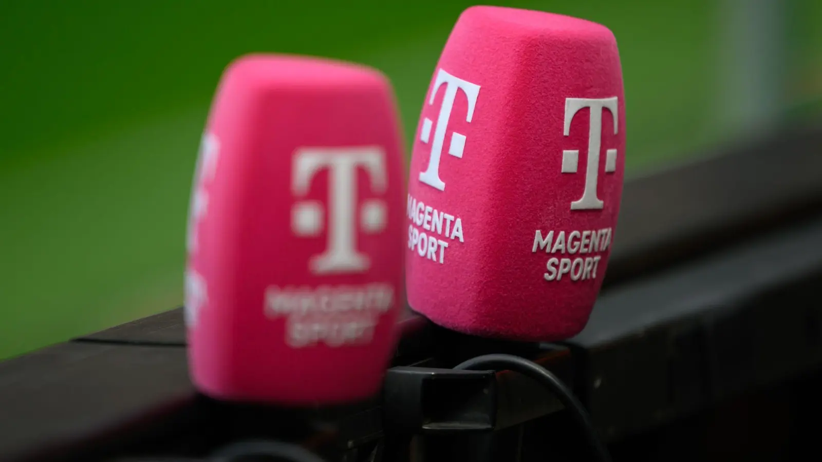 Zwei Mikrofone von Magenta Sport stecken an einer Bande bei einem Fußballplatz. (Foto: Robert Michael/dpa)