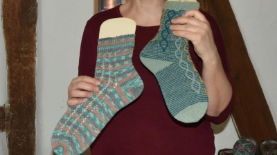Gruppenleiterin Heike Madiar zeigt grüne Socken. Das linke Exemplar hat eine Zunahmeferse, die rechte eine Bumerangferse. (Foto: Anita Dlugoß)