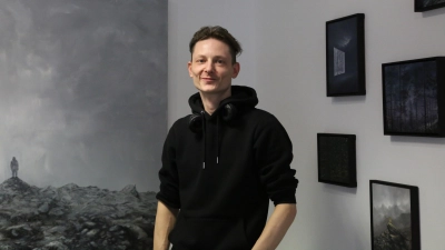 Der Maler Jan Gemeinhardt inmitten seiner stillen, weiten, oft düsteren und geheimnisvollen Landschaften: In der Ausstellung in Heilsbronn sind viele Entdeckungen möglich. (Foto: Martina Kramer)