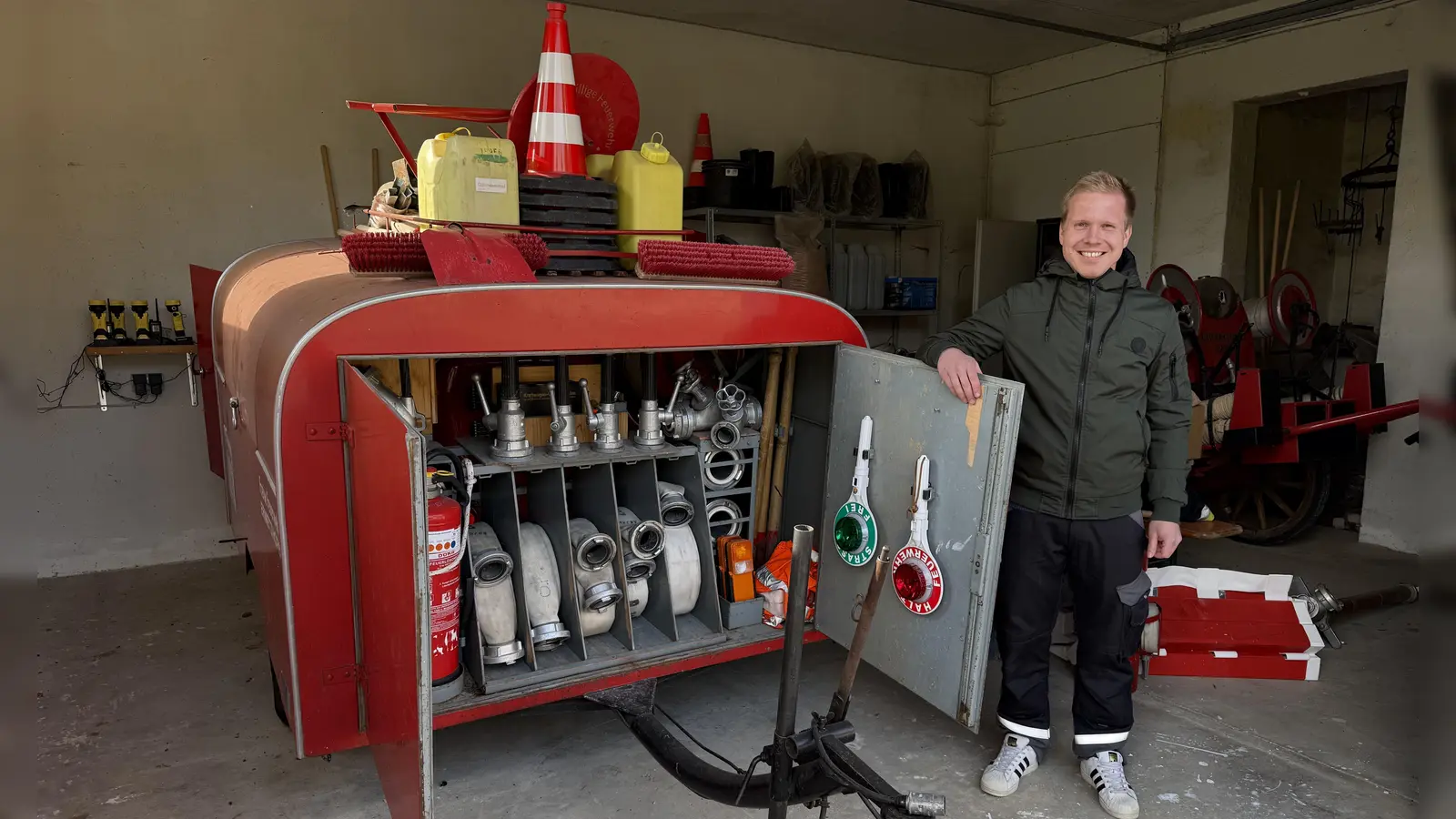 Im seit 1969 bestehenden Feuerwehrhaus ist lediglich Platz für diesen kleinen Spritzenanhänger, den Jens Geuder hier zeigt. Für ein Auto ist das Haus zu klein. Dieser Anhänger wird daher vom ersten Traktor, der nach der Alarmierung eintrifft, zum Brandplatz geschleppt. (Foto: Sylvia Fehlinger)