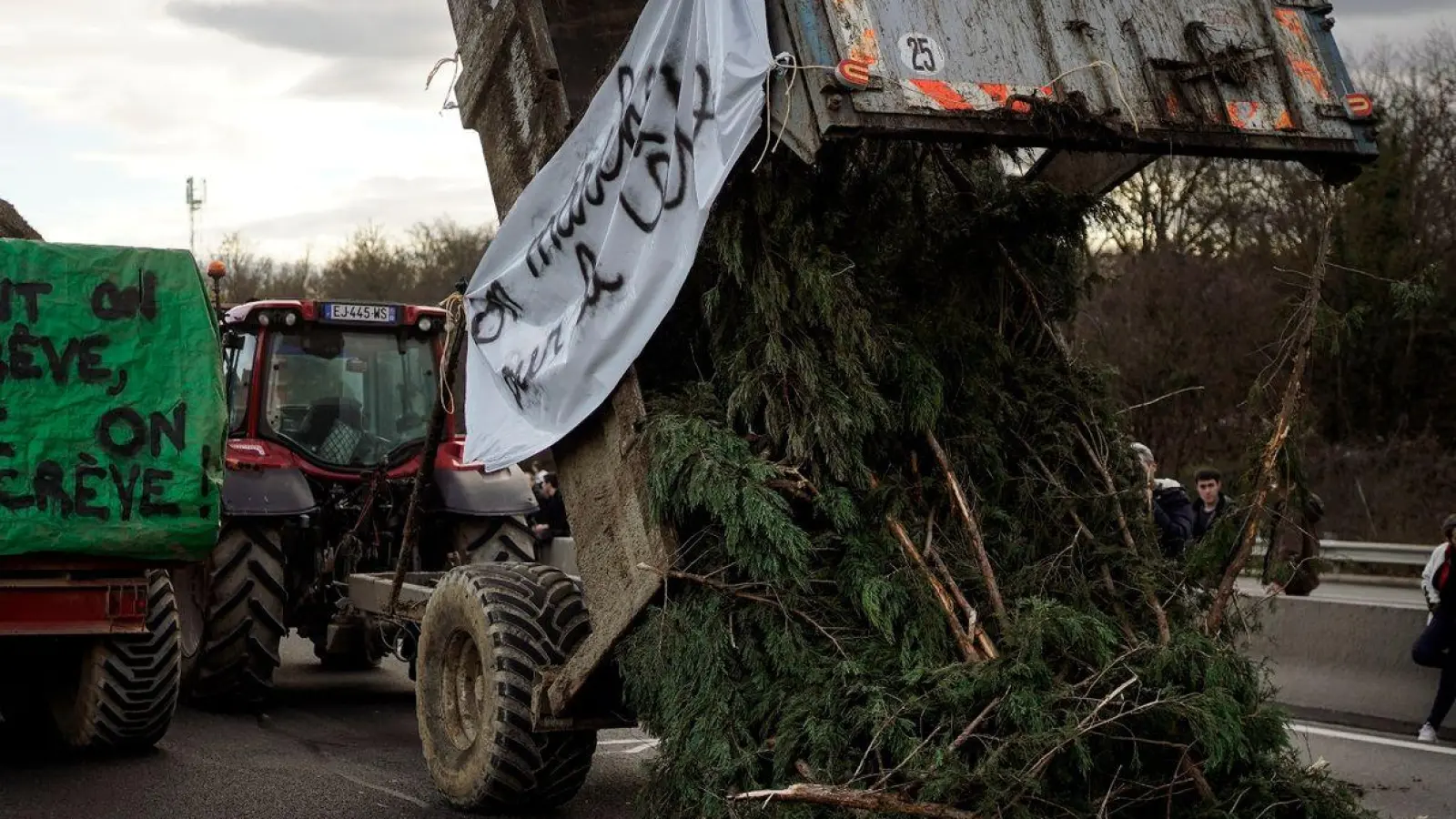 Landwirte kippen Zweige und Äste auf die Fahrbahn, während sie eine Autobahn in der Nähe von Lyon blockieren. (Foto: Laurent Cipriani/AP/dpa)