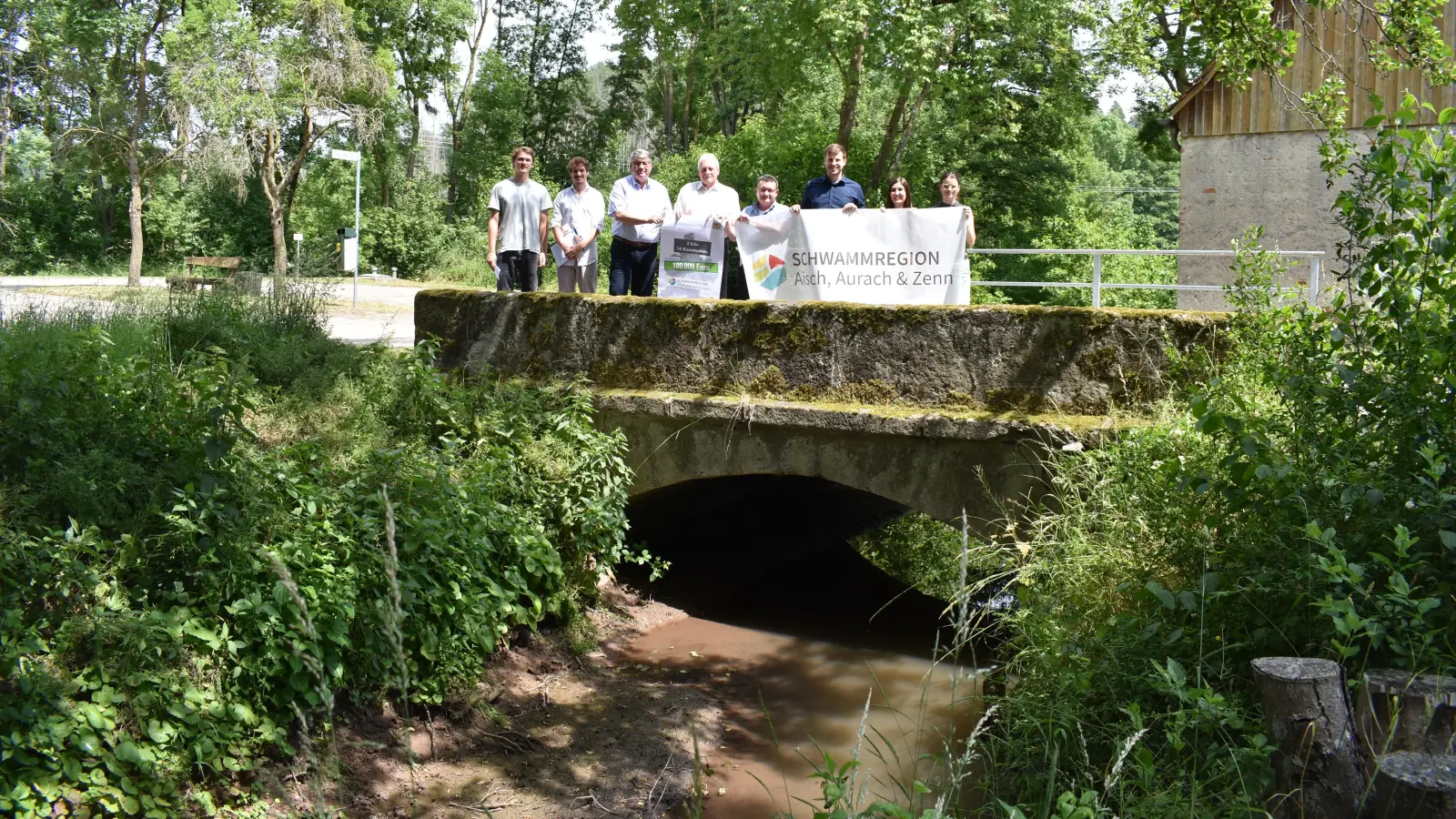 Zum Thema Schwammregion fand ein Pressetermin in Steinbach statt. Die Brücke, auf der die Teilnehmer stehen, wurde beim Starkregen enorm beschädigt, Gebäude standen meterhoch unter Wasser. (Foto: Ute Niephaus)